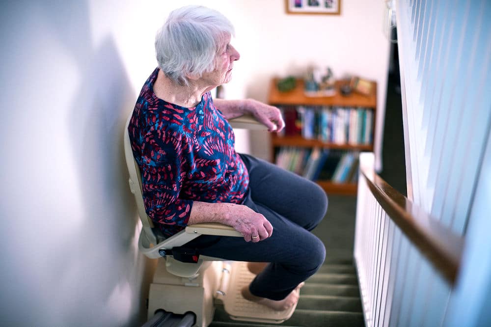 Seniorin sitzt im Treppenlift.